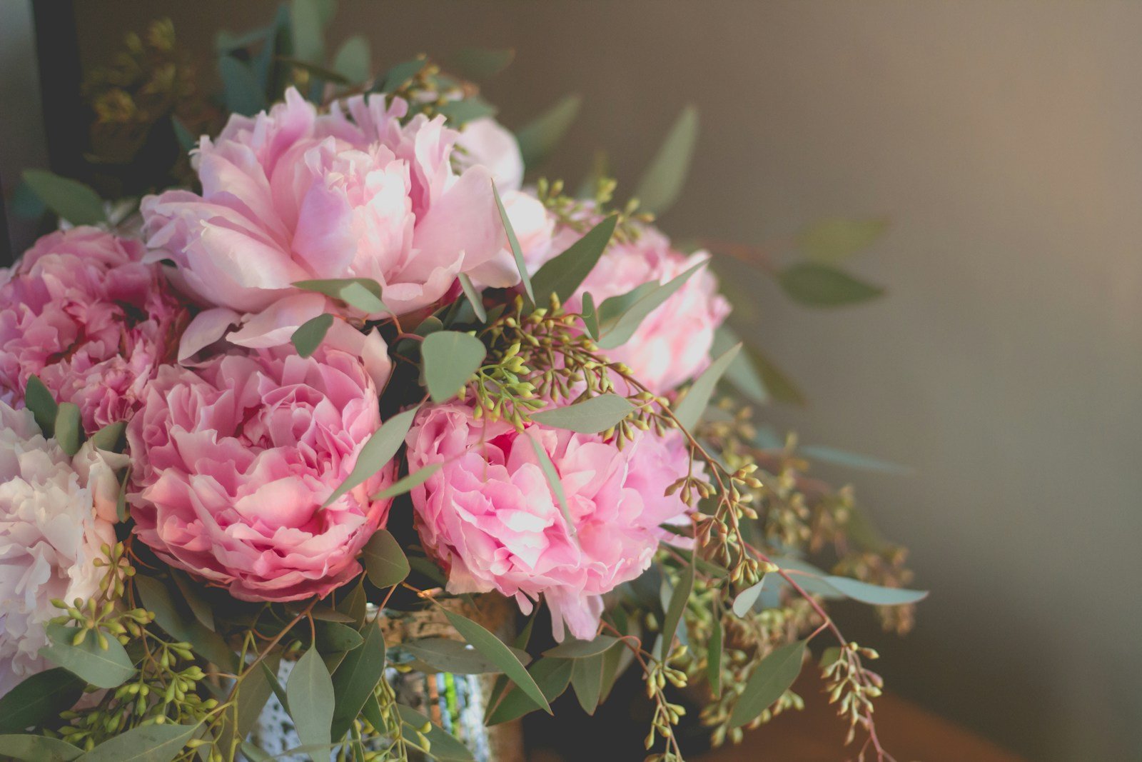 A bouquet of pink peonies and green eucalyptus leaves sits against a soft, blurred background.